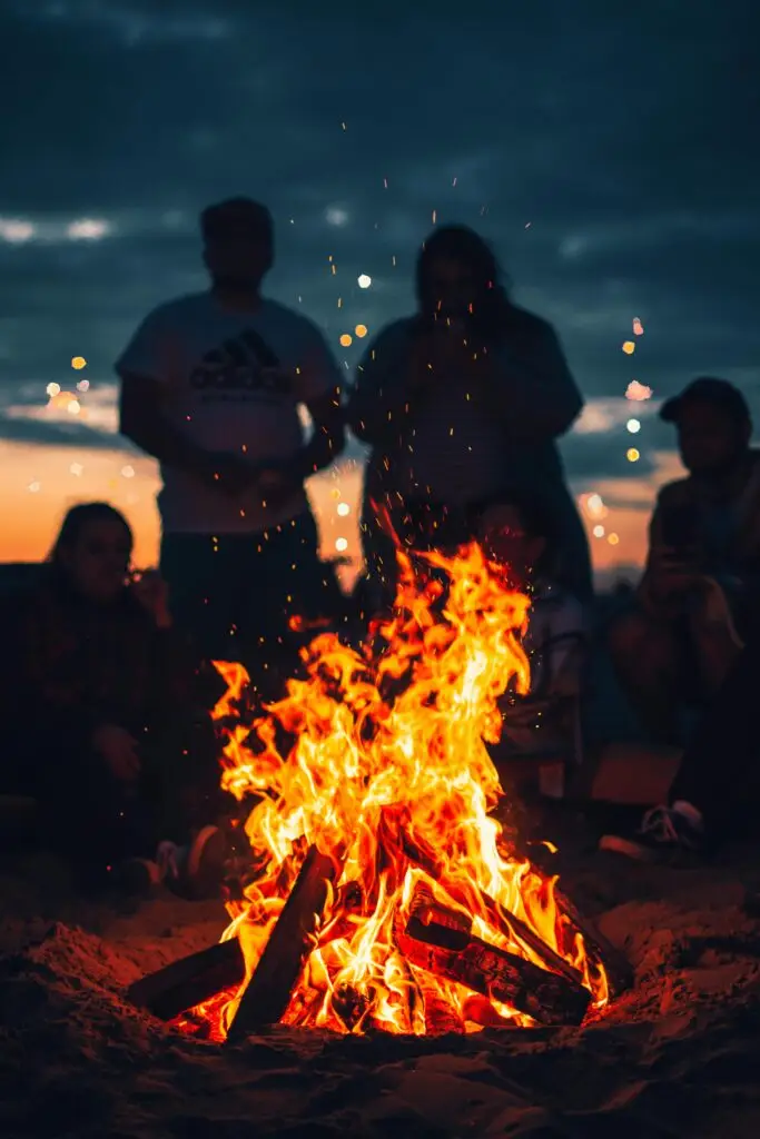 A group of friends enjoying a bonfire on the beach at twilight, creating a warm and inviting atmosphere.