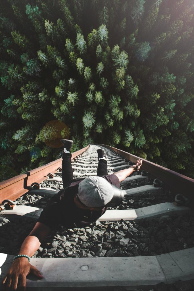 A man poses daringly over train tracks with a forest view.